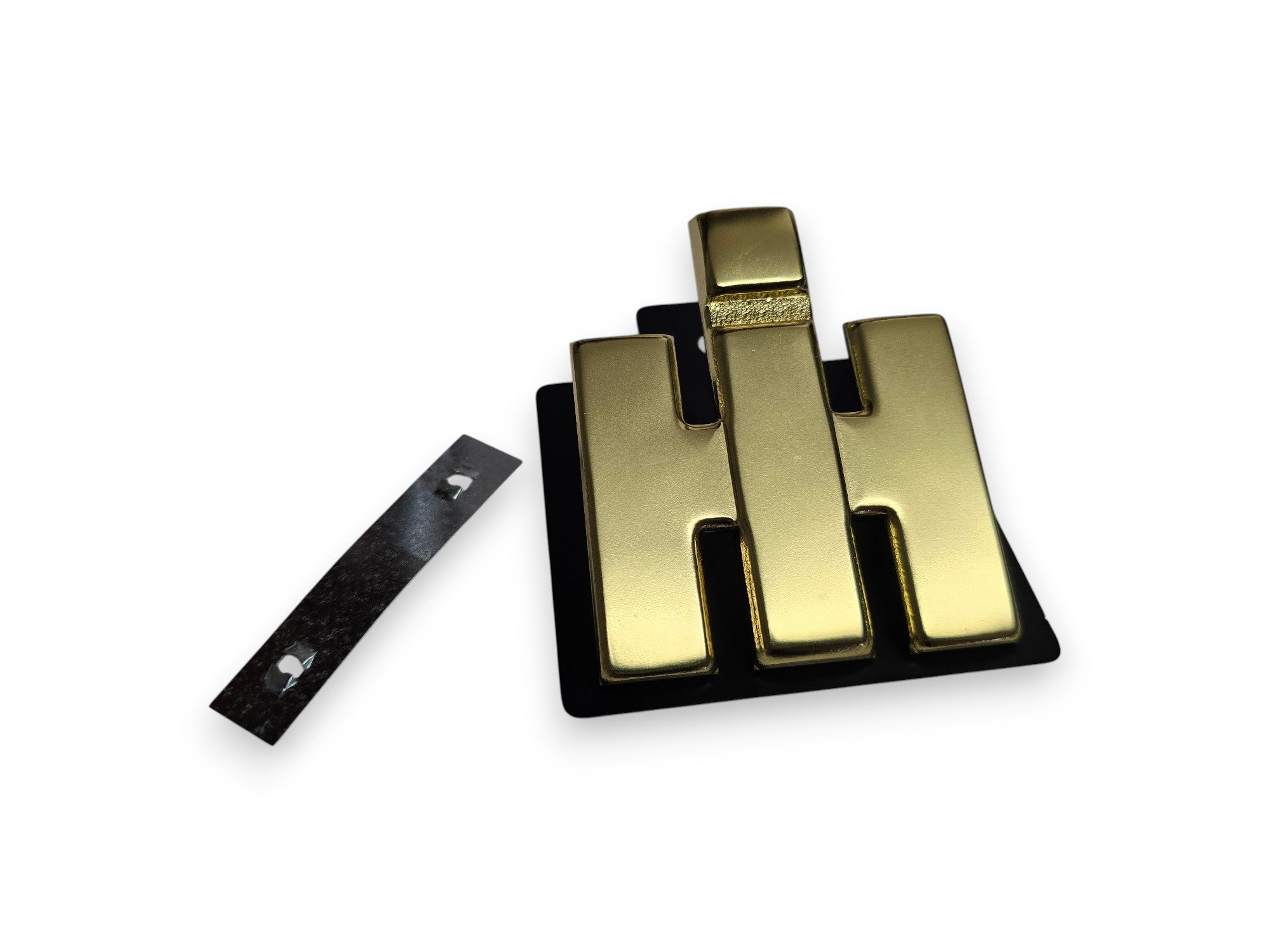 A gold-colored metal H-shaped badge or emblem with a black backing, shown alongside a separate black strip with two small silver dots, on a plain white background.